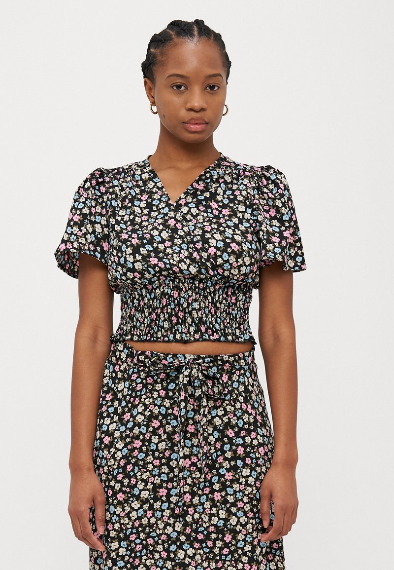 Cropped top nero floreale con maniche a sbuffo, dotato di vita arricciata e scollatura a V. Piccole fiori multicolori in rosa, blu e bianco.