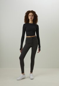 Svart langermet crop topp kombinert med mørkegrå skinny jeans og hvite sneakers. Glatt stoff med tettsittende design og hull for tomlene i ermene.