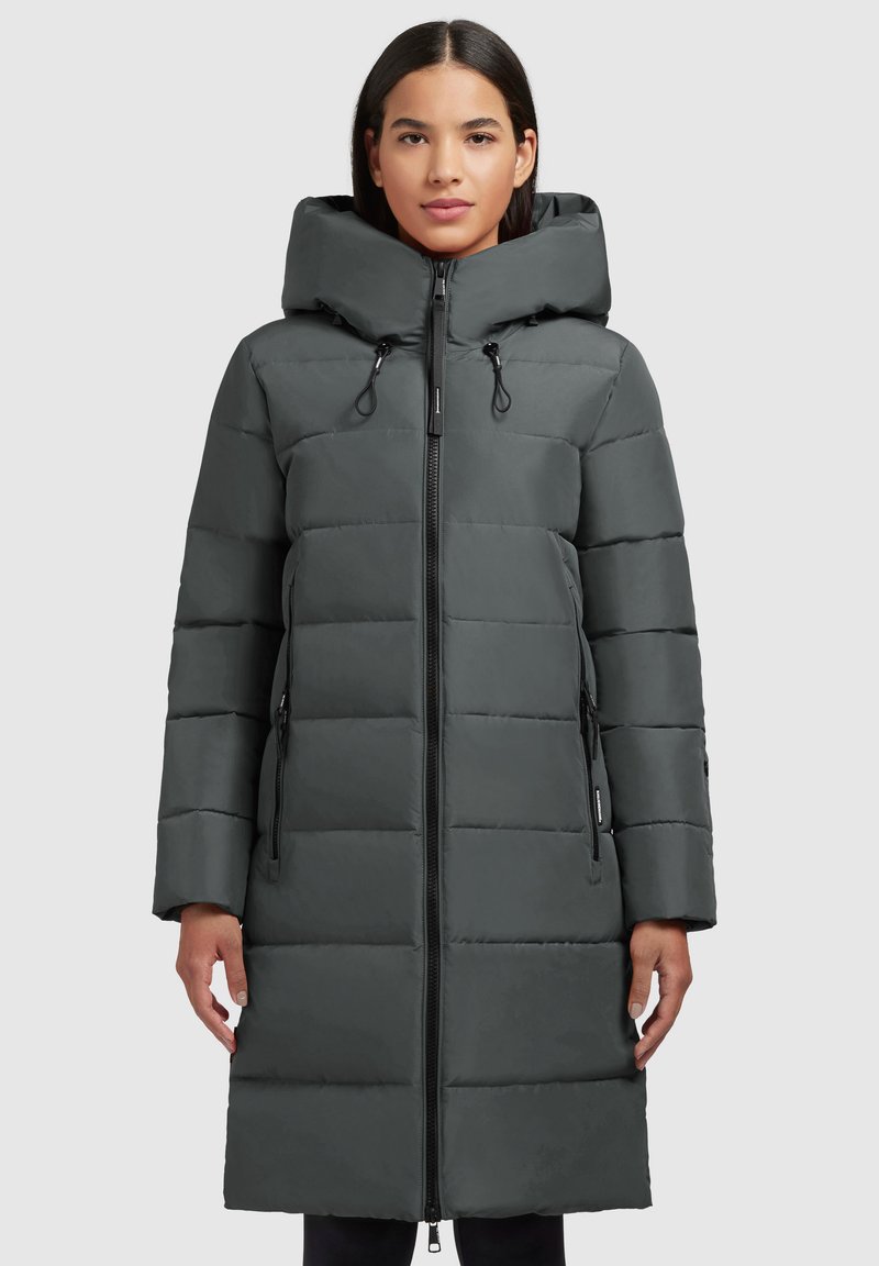 Parka matelassée grise avec un col haut, fermeture éclair devant et capuche à cordon de serrage réglable. Elle dispose de poches latérales et d'un design longueur genou.