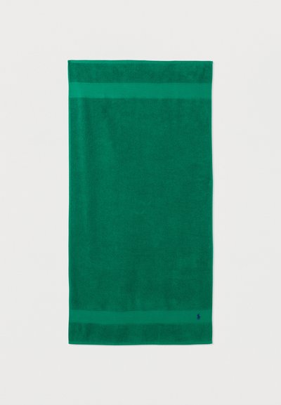 Σκούρα πράσινη ορθογώνια πετσέτα με δύο οριζόντιες λωρίδες κοντά στις άκρες και μικρό κεντημένο λογότυπο στη κάτω γωνία.