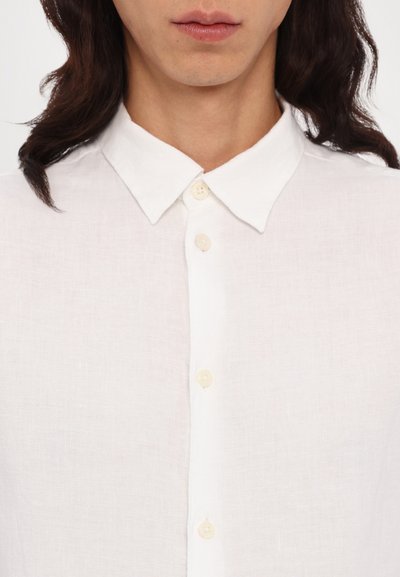 White linen shirt featuring a classic collar, button closure, and a textured fabric. Buttons are cream-colored and subtly stitched.