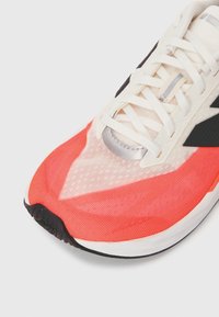Running shoe in coral and white, featuring a mesh upper, soft texture, black accents, and a distinctive triangular design on the side.