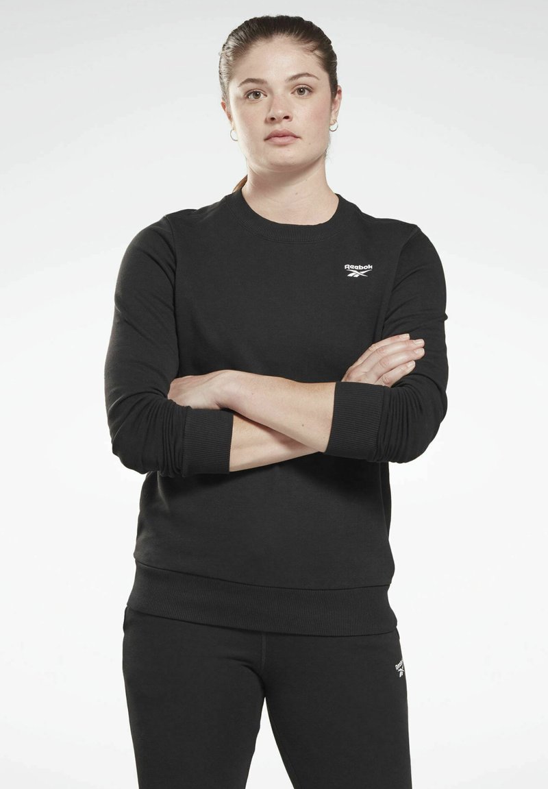Crna dukserica s okruglim izrezom, rebrastim manžetama i rubom, s malim Reebok logotipom na lijevoj strani prsnog koša. Glatka tekstura i prilagođeni dizajn.