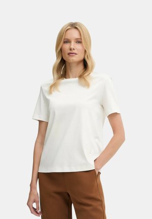 Maglietta bianca a maniche corte con scollo rotondo, caratterizzata da una texture liscia e dettagli sottili. Abbinata a pantaloni marroni.