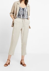 Beige blazer över mönstrad ormtryckt topp, ljusa linbyxor och bruna klacksandaler. Avslappnat outfit med en lös passform och dragsko i midjan.