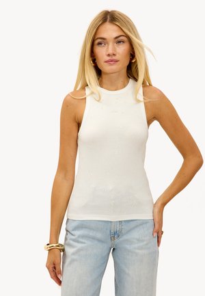 Weißes geripptes Tanktop mit hohem Halsausschnitt, verziert mit strukturierten Perlen auf der Vorderseite. Kombiniert mit hellblauen Jeans.