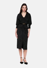 Black dress with textured pattern, fitted silhouette, v-neck, and long sleeves. Belted at the waist with a decorative snake-shaped buckle.