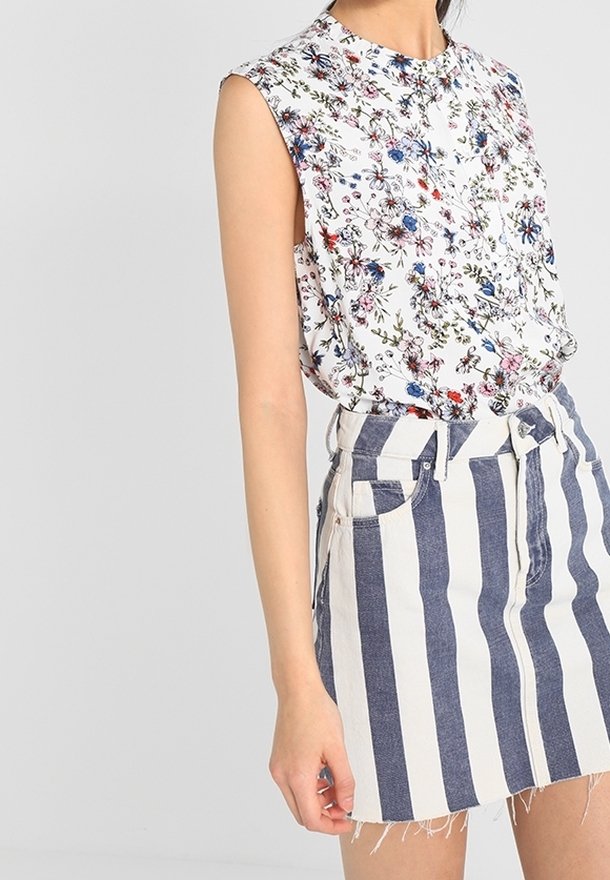 Blusa senza maniche floreale con collo alto, abbinata a una gonna di jeans a vita alta con strisce verticali blu e bianche.