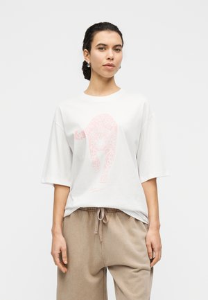 Hvid bomuldst-shirt med pink leopardgrafik, korte ærmer og en afslappet pasform. Båret med beige joggingbukser.