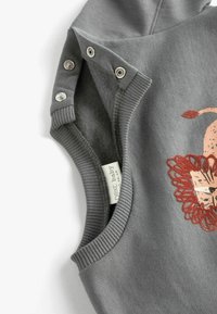 Grå ærmeløs babybeklædning med en blød tekstur, prydet med et dekorativt orange dyremotiv, metaltrykknapper og ribbede armhuller.