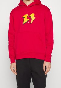 Sudadera de algodón roja con bolsillo frontal, puños de canalé y gráfico de rayo amarillo con contorno negro en el pecho.