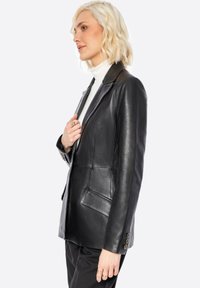 Zwarte leren blazer met notch revers, twee voorkzakken en knopen bij de manchetten. Soepele textuur en getailleerde pasvorm.