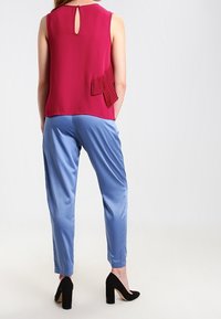 Červený top bez rukávů s klíčovou dírkou vzadu a okrasnými sklady. Světle modré saténové kalhoty se zúženým střihem. Černé vysoké podpatky.