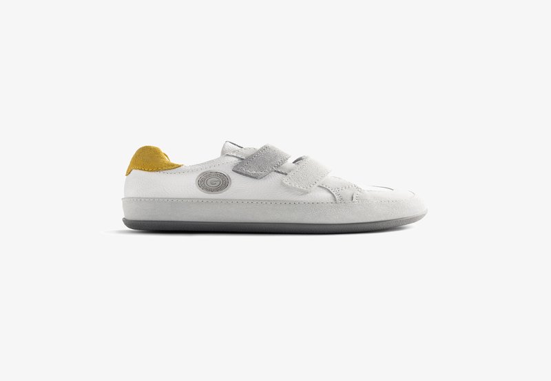 Scarpa bianca in pelle con dettagli in camoscio grigio e giallo, dotata di due fasce in Velcro e un logo circolare grigio sul lato.