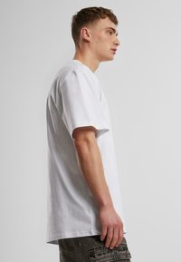T-shirt en coton blanc avec une coupe décontractée, des manches courtes et un col rond. Le tissu semble lisse avec des coutures minimales.