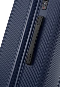 Námořnický hardshell kufr s texturovanými vertikálními pruhy, černou rukojetí a kombinovaným zámkem, vybavený hladkým zipem a odolným designem.