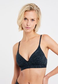 Sort og mørkegrå zebra-mønstret bralette med v-halsdesign, justerbare stropper og en glat tekstur. Subtil branding på siden.