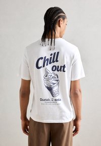 Biała bawełniana koszulka z krótkim rękawem, z dużą niebieską grafiką lodów w rożku oraz napisem "Chill out" na plecach, o klasycznym kroju.