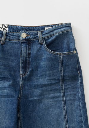 Dunkelblaue Jeans aus Denim mit einem klassischen Fünf-Taschen-Design, Metallknopfverschluss und subtilen Verfärbungen im Stoff.