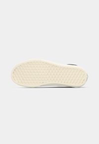 Sole of a black and white sneaker showing diamond-patterned beige rubber outsole with waffle-like texture.