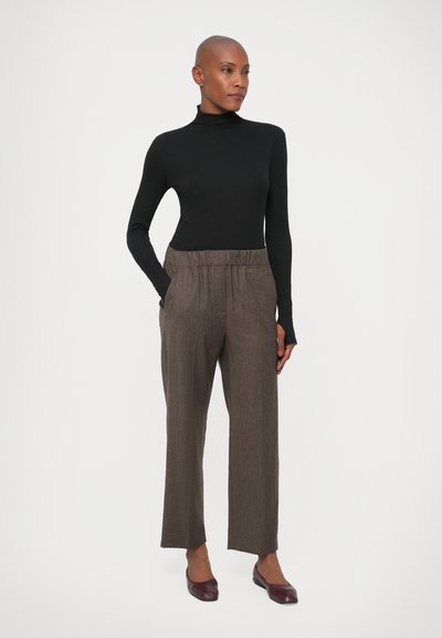 Cămașă neagră cu guler înalt, design ajustat. Pantaloni cu model în carouri maro, cu talie elastică și buzunare laterale. Asortați cu pantofi burgundii.