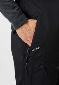 Black outdoor pants with a zippered pocket, made from water-resistant material. Features STX™ 8000 branding and durable zippers.