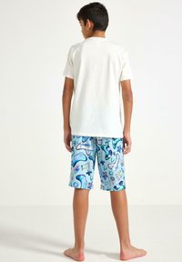 Korte mouwen witte T-shirt gecombineerd met blauwe short met patronen, featuring gaming graphics, geometrische vormen en een gladde textuur.