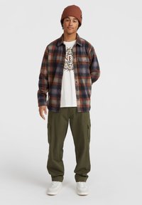 Rutig flannel skjorte i navy, orange og creme farver, lagd oven på en hvid grafisk t-shirt. Olivenfarvede cargo bukser og hvide sneakers fuldender outfittet.