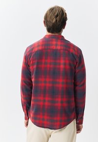 Cămașă din flanel în carouri roșii și bleumarin, cu mâneci lungi, manșete cu nasturi și tiv rotunjit, confecționată dintr-un material texturat.