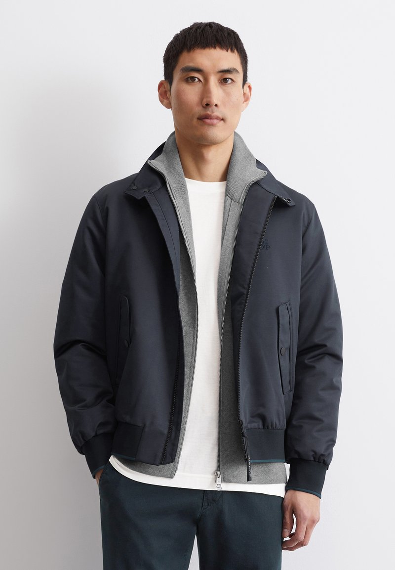 Tamsiai mėlyna bombonešio striukė su pilku vidiniu pamušalu, priekinėmis kišenėmis ir užtrauktuku. Pagaminta iš sklandaus, lengvo audinio.