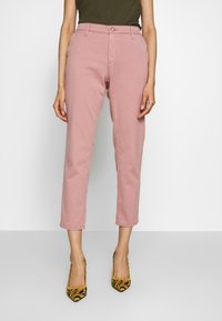 Ljusrosa byxor i bomullsblandning, med smal passform, cropped längd och frontknäppning, kombinerade med mönstrade gula klackar.