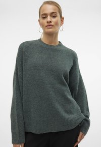 Tmavě zelený, oversized svetr vyrobený z měkkého, texturovaného materiálu. Má kulatý výstřih a žebrovaný lem a manžety. Jednoduchý design, bez vzorů.