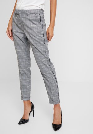 Pantalons gris à carreaux avec une coupe fuselée, présentant des rayures latérales noires et une texture lisse. Portés avec des chaussures à talons hauts noires.