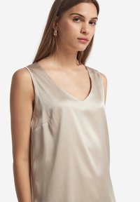 Beige satin ärmlös topp med V-ringning, med en subtil lyster och en avslappnad passform. Inkluderar en ficka i sidan för funktionalitet.