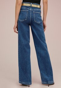 Jean en denim à jambe large, de couleur bleu foncé avec une texture lisse. Présente une ceinture dorée et deux poches arrière avec des détails de couture contrastants.