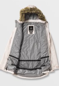 Veste d'hiver avec capuche en fourrure, extérieur clair, doublure intérieure grise à motifs, et étiquette Volcom sur la zone du cou.