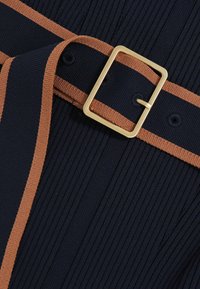 Marineblauwe geplooide stof met een contrasterende bruine riem. De riem heeft een rechthoekige gouden gesp en bijpassende stiksels langs de randen.