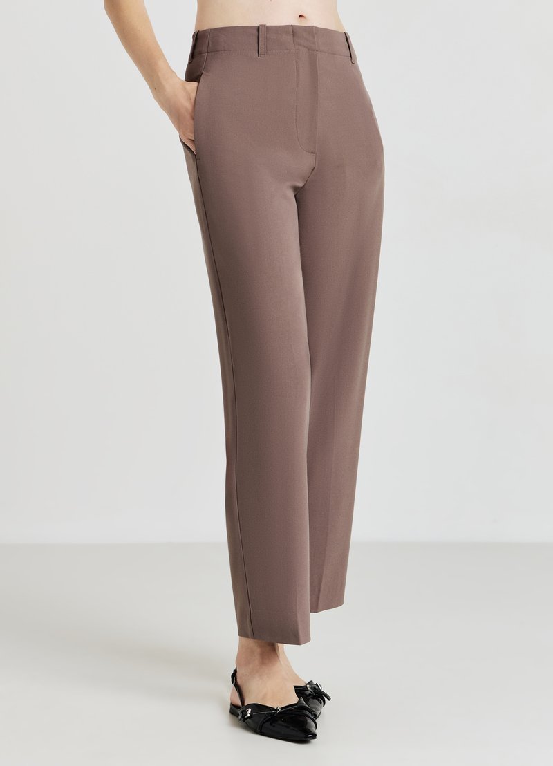 Braune maßgeschneiderte Hose mit glatter Textur, geradem Schnitt und Eingrifftaschen. Getragen mit schwarzen Lackschuhen mit einer Schleifenapplikation.