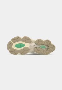 Athletic shoe outsole featuring a combination of beige and green rubber, with a textured surface and unique tread pattern for grip.