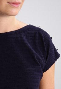 Top azul marino de manga corta con rayas horizontales texturizadas; cuenta con botones decorativos en los hombros, escote redondo y tela suave.