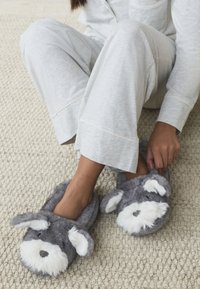 Graue, pelzige Hausschuhe, gestaltet wie ein Hund, mit weißen Akzenten an Ohren und Schnauze. Weiche Textur, Schlupfstil, geeignet für den Innenbereich.