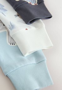 Three ribbed cuffs in varying colors: dark grey, white, and light blue. The fabrics are soft and feature subtle designs and textures.