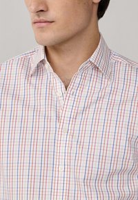 Chemise à carreaux avec une base blanche ornée de motifs à carreaux rouges et bleus, fermeture à boutons à l'avant et col standard. Tissu doux et tissé.