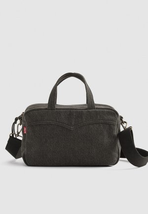 Bolso compacto de tela gris oscuro con dos asas superiores, correa de hombro negra desmontable y detalle sutil de costura en la parte frontal.