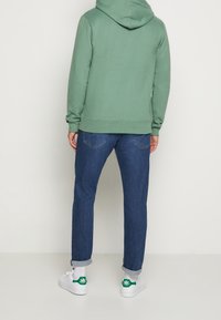 Grön hoodie med textilier med struktur, blå jeans och vita sneakers med gröna detaljer. Utseendet är avslappnat och ledigt.