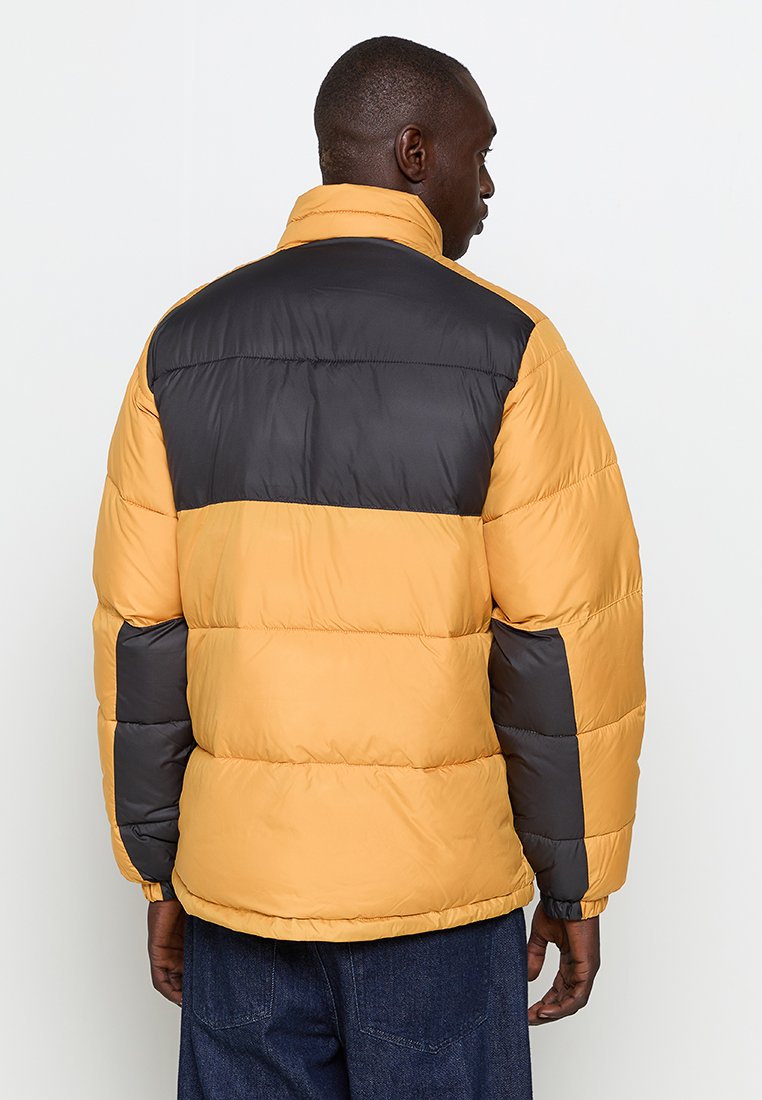 Chaqueta tipo abrigo de plumas con un cuerpo amarillo y una sección superior y mangas negras, textura acolchada, cuello alto y puños elásticos para mayor calidez.