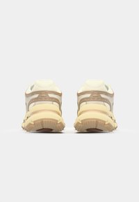 Vue arrière de chaussures de sport beiges avec des accents texturés, une semelle jaune et un rembourrage vert clair au niveau du col et de la languette.