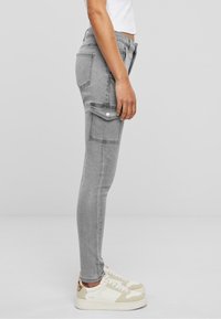 Sivi traper skinny cargo hlače s bočnim džepovima, prilagođenim siluetom i glatkom teksturom, uparenim s svijetlim ležernim tenisicama.