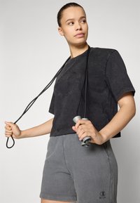 Black cropped t-shirt with embossed logo, paired with gray ribbed shorts. Model holds a gray jump rope with black handles.