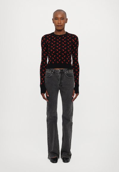 Černý pletený svetřík s červenými crescentovými vzory, kombinovaný s tmavě šedými rozšířenými džíny. Oblečení má těsné rukávy a zkrácenou délku.